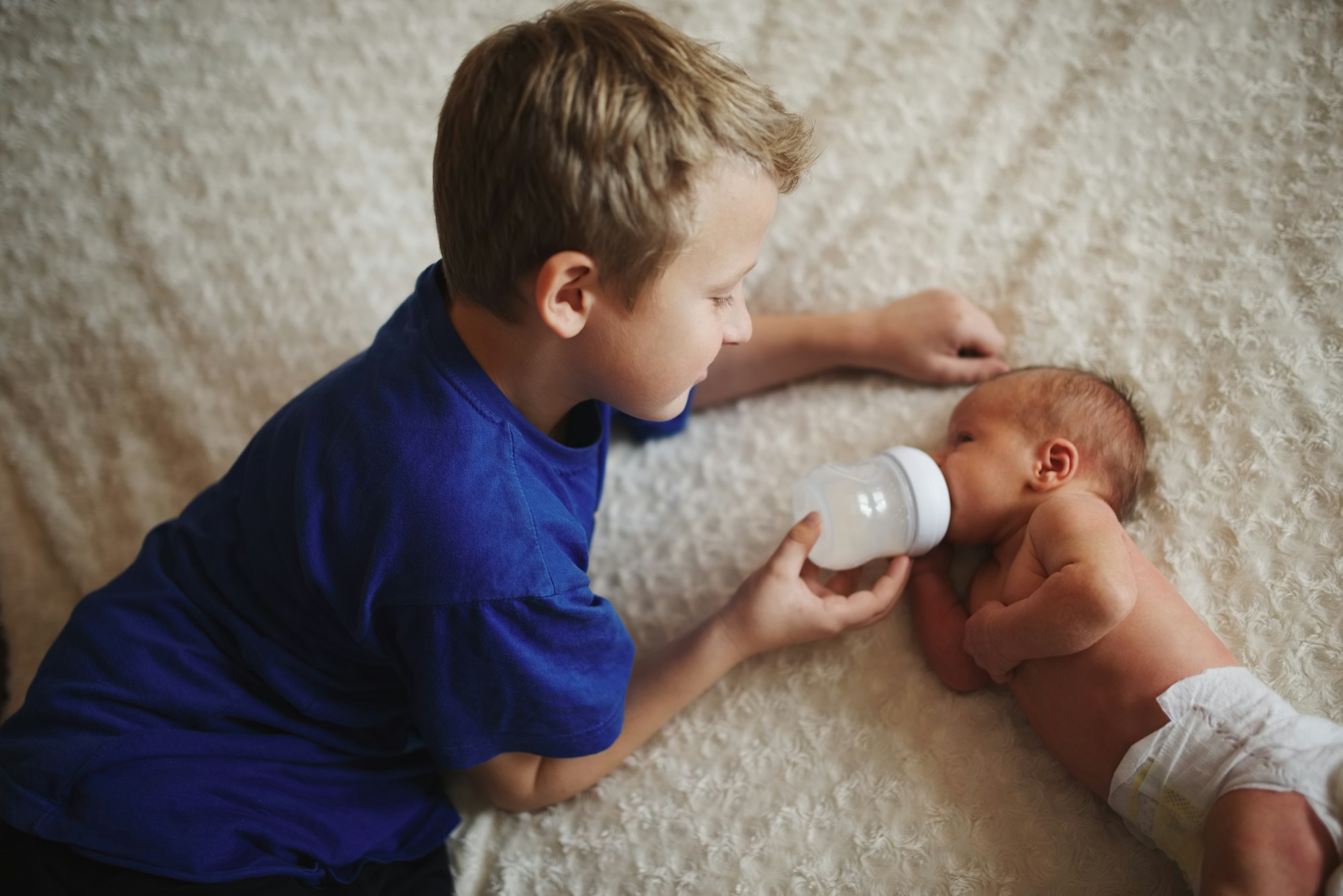 boy feeding newborn baby with bottle of milk