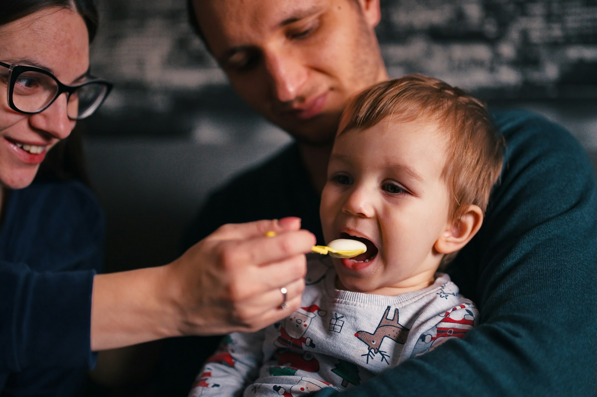 Parents sitting on a sofa and feeding their little boy